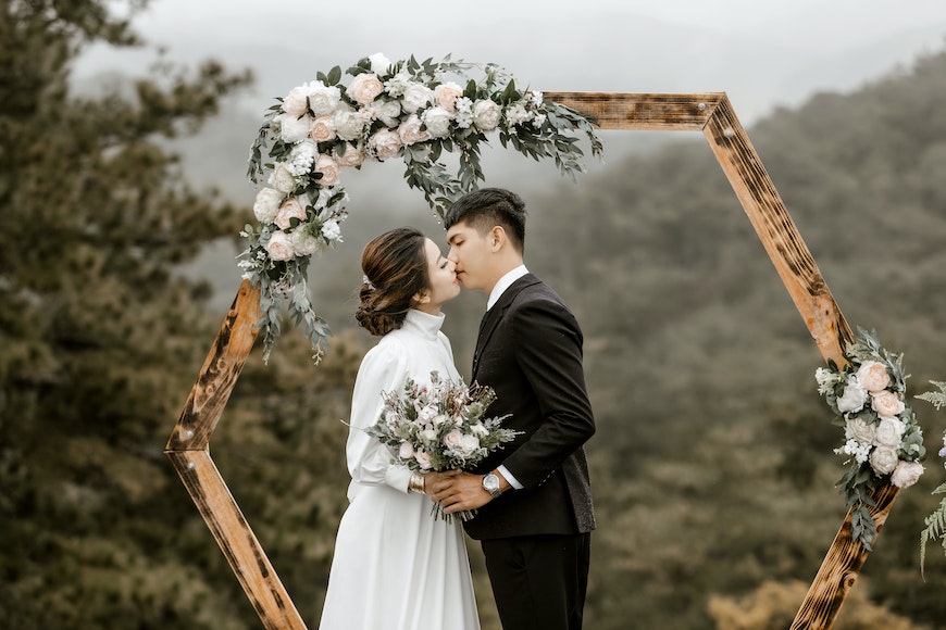 A bride and groom kiss in front of a hexagonal wedding arch.