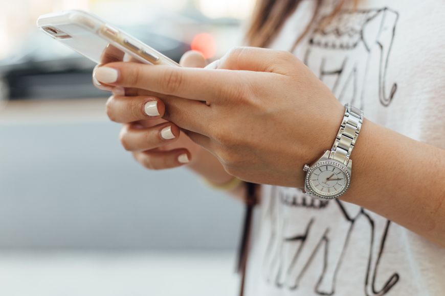 A woman holding a cell phone while looking at her watch.