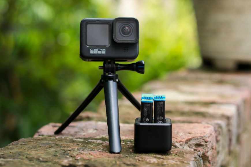 A Gopro hero with a battery and charger on a brick wall.