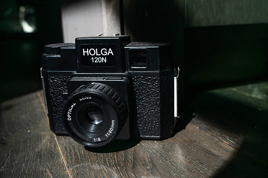 A black holga camera sits on a wooden floor.
