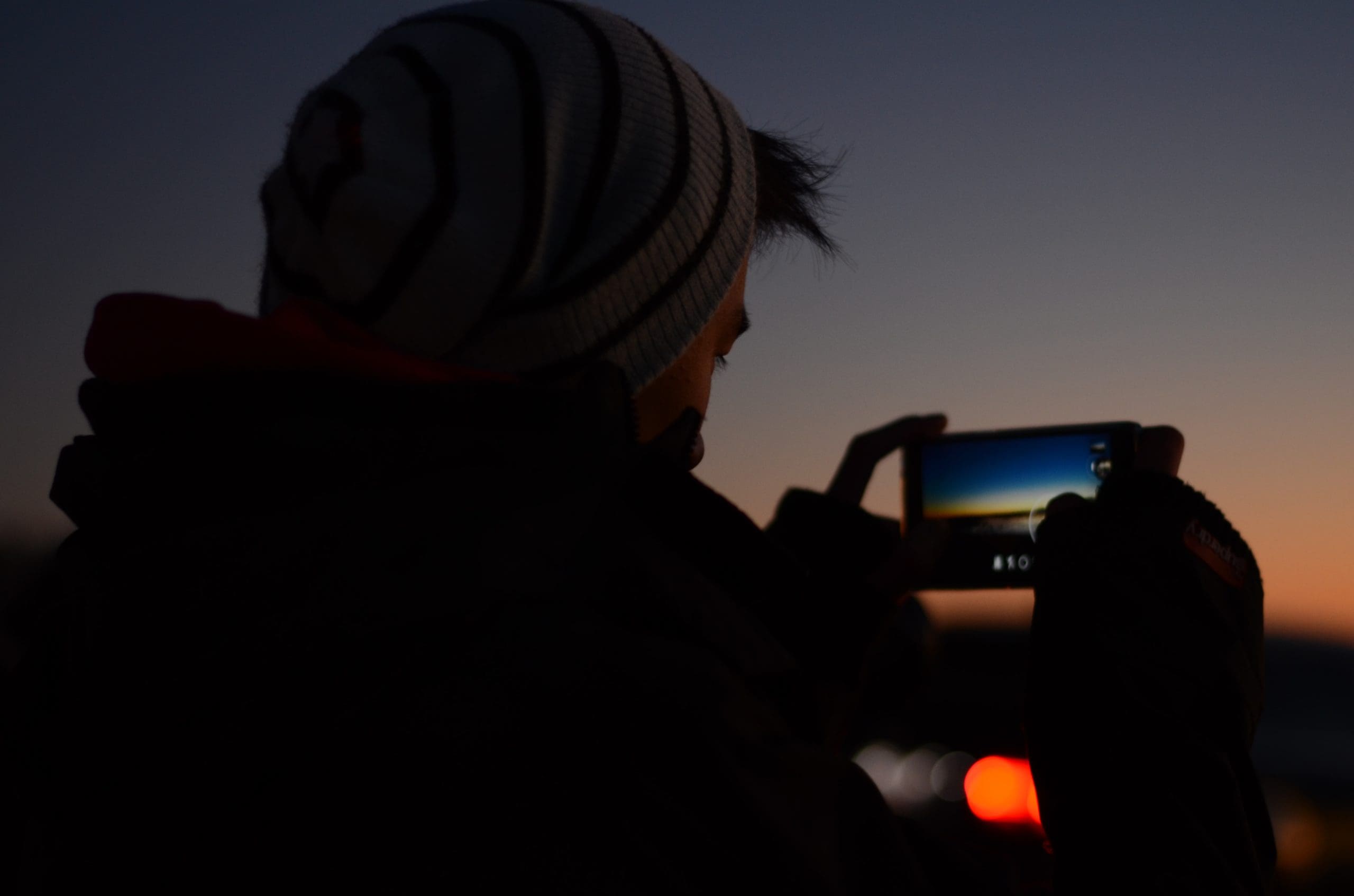 A person taking a picture of the sunset with a cell phone.