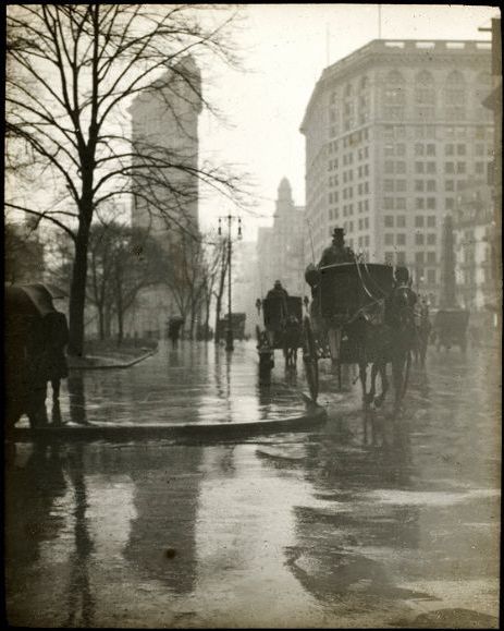 An old photo of a horse drawn carriage on a wet street.