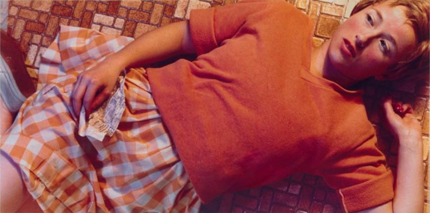 A woman laying on a tile floor in a plaid skirt.