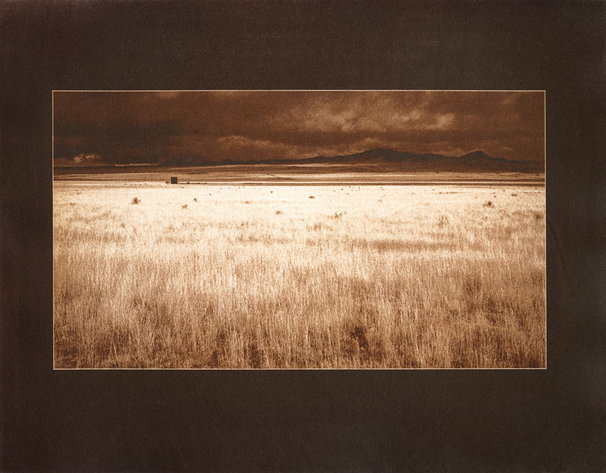 A sepia photo of a field with mountains in the background.