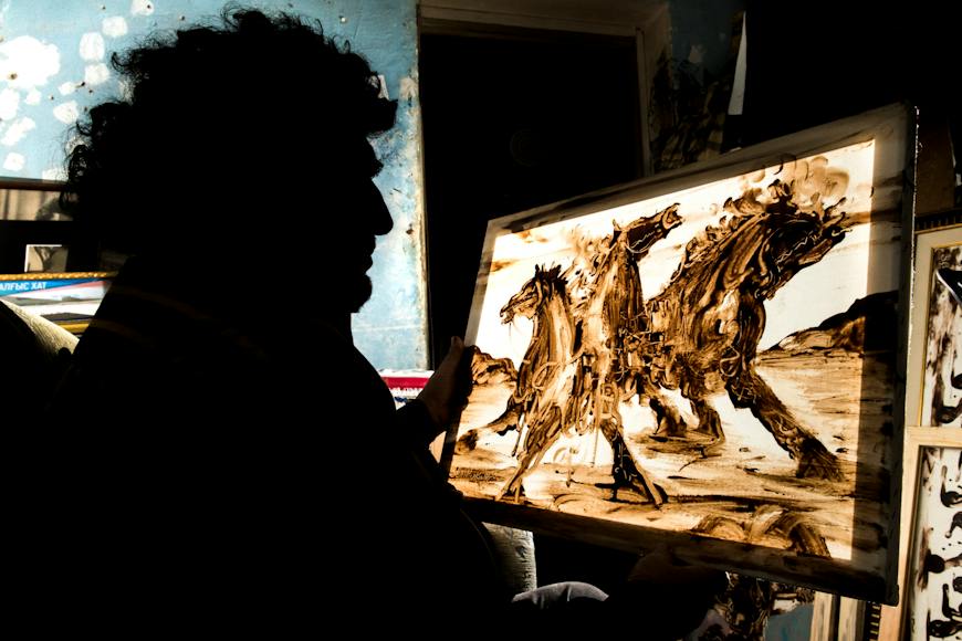 A man holding a painting of horses in the dark.