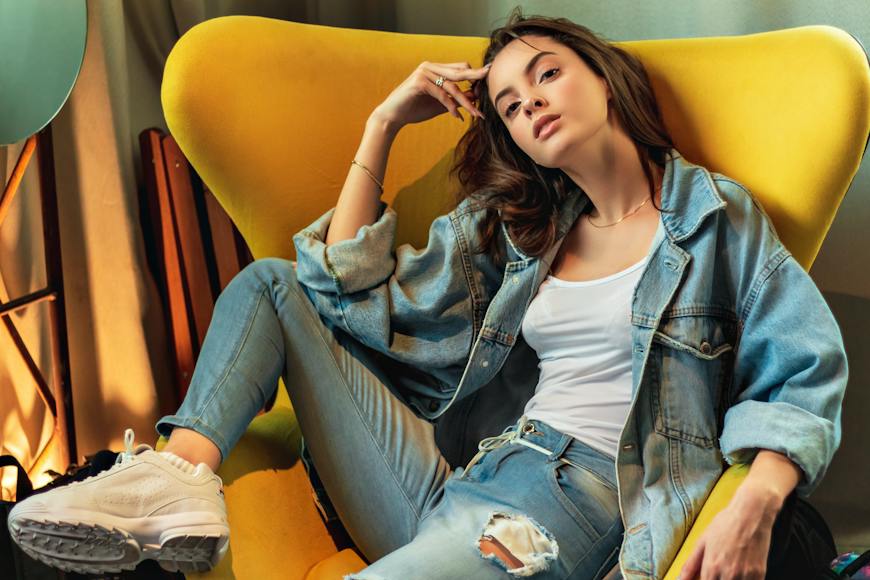 A woman in a denim jacket sitting on a yellow chair.
