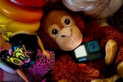 A teddy bear laying next to a doll and balloons and a lost GoPro camera.