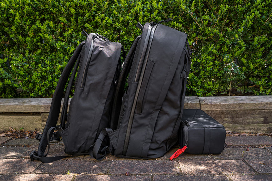 Two black backpacks sitting next to each other on a sidewalk.