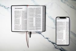 An open bible and a smartphone on a marble surface.