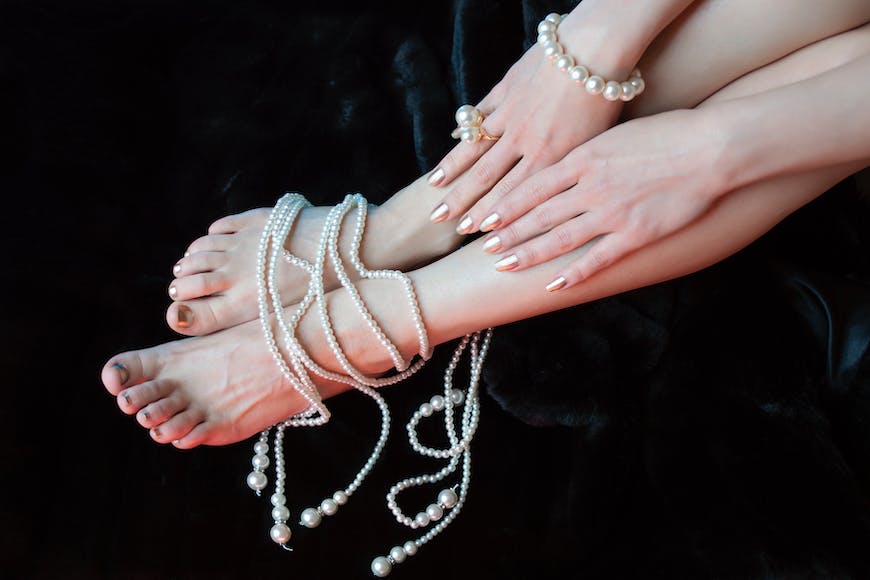 A woman's bare feet with pearls and chains on a black background.