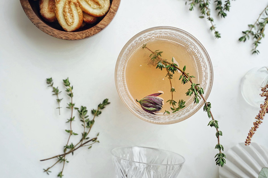 A glass of a drink with a sprig of thyme.