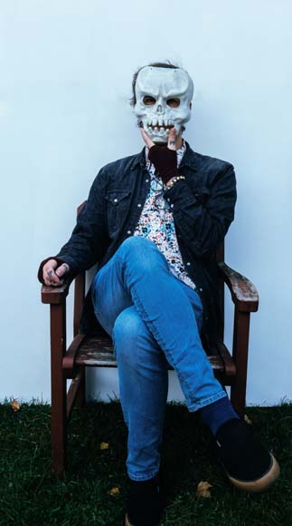 A man sitting in a chair with a skull mask on his face.