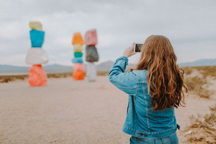 A woman taking a picture of colorful rocks in the desert.