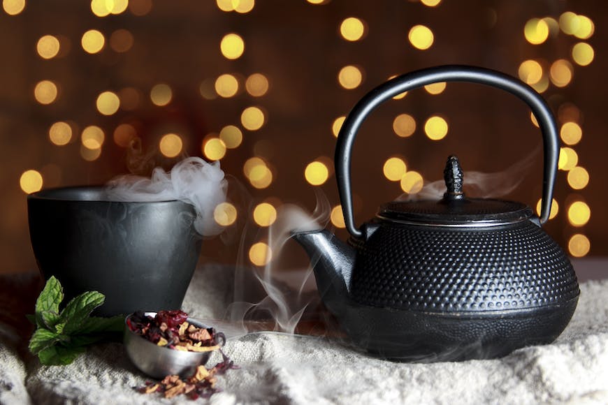 A black teapot on a table next to a cup of tea.