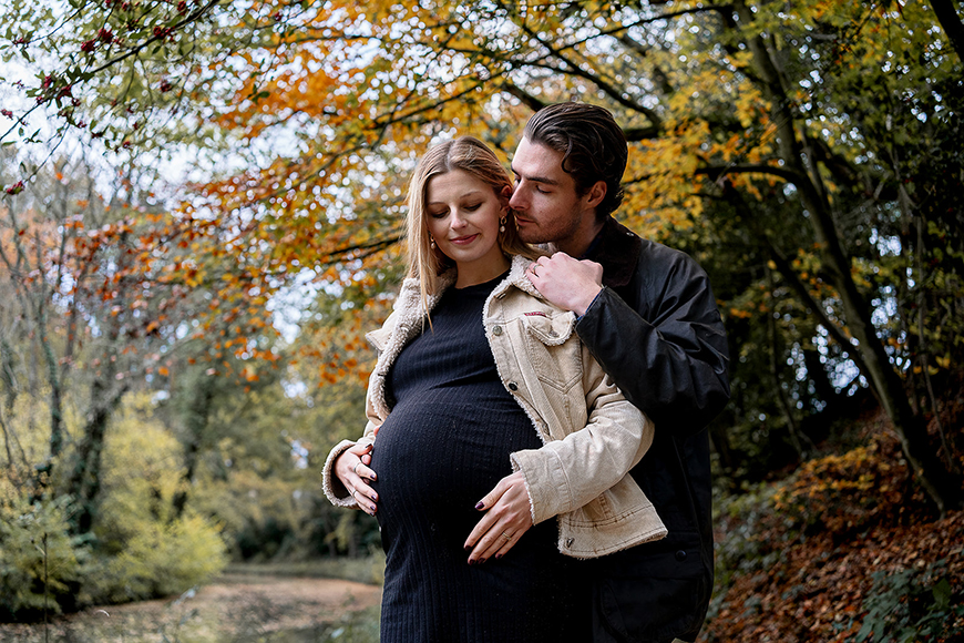 A pregnant couple embracing in the autumn leaves.