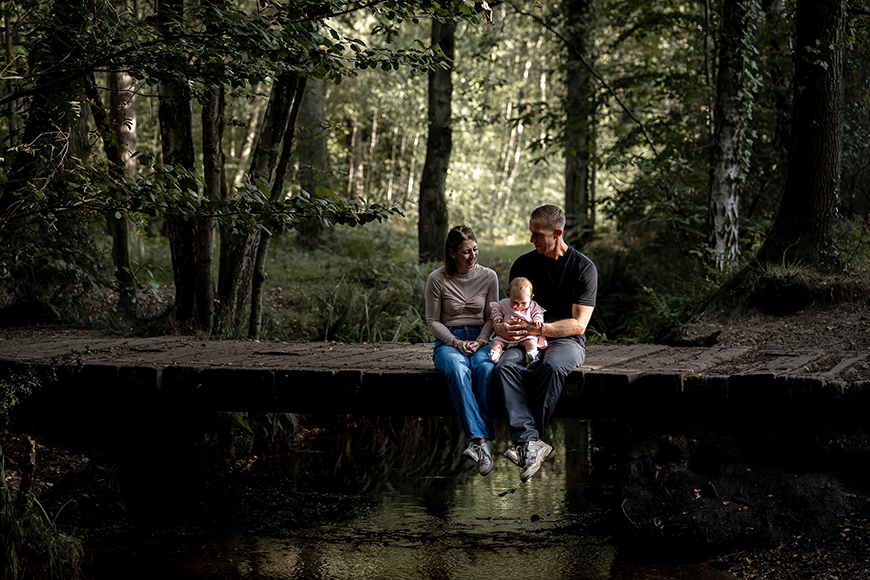 A man and woman sitting on a wooden bridge in the woods.