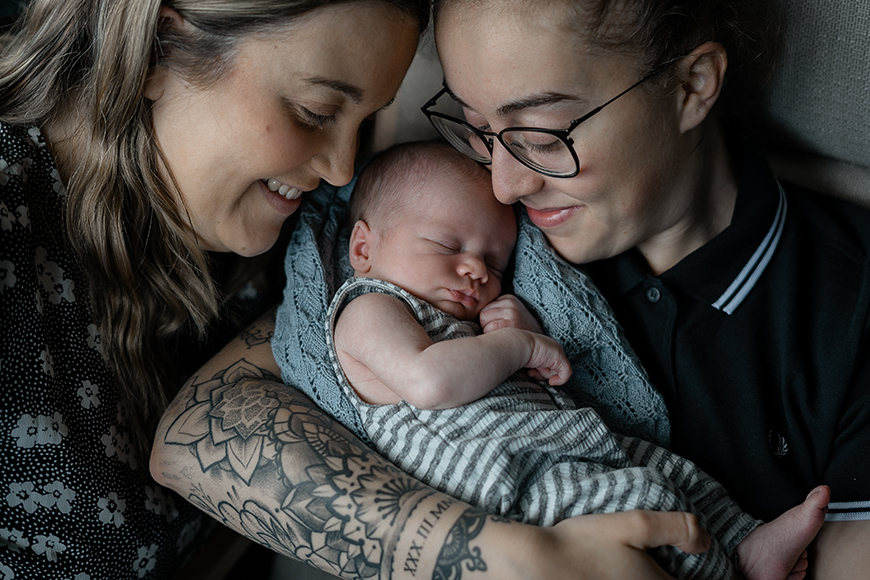 Two women holding a baby with tattoos.