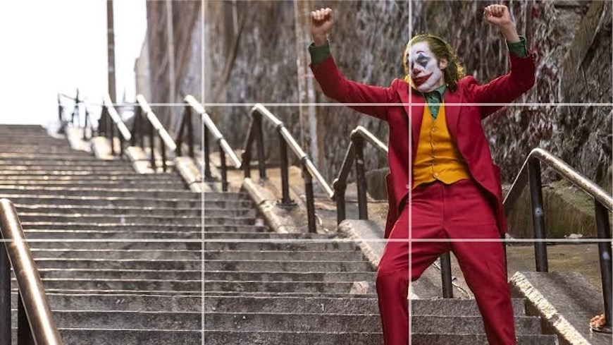 A joker is standing on a set of stairs.