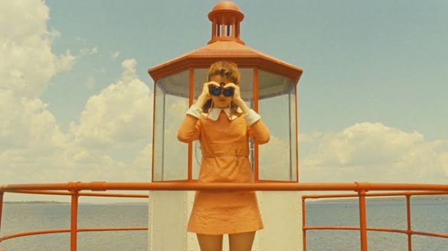 A woman in an orange dress standing on top of a lighthouse.