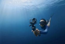 A woman in a wetsuit holding a gopro underwater.
