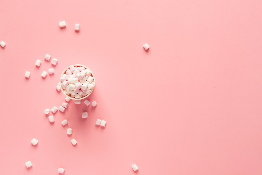 A cup of white marshmallows on a pink background.