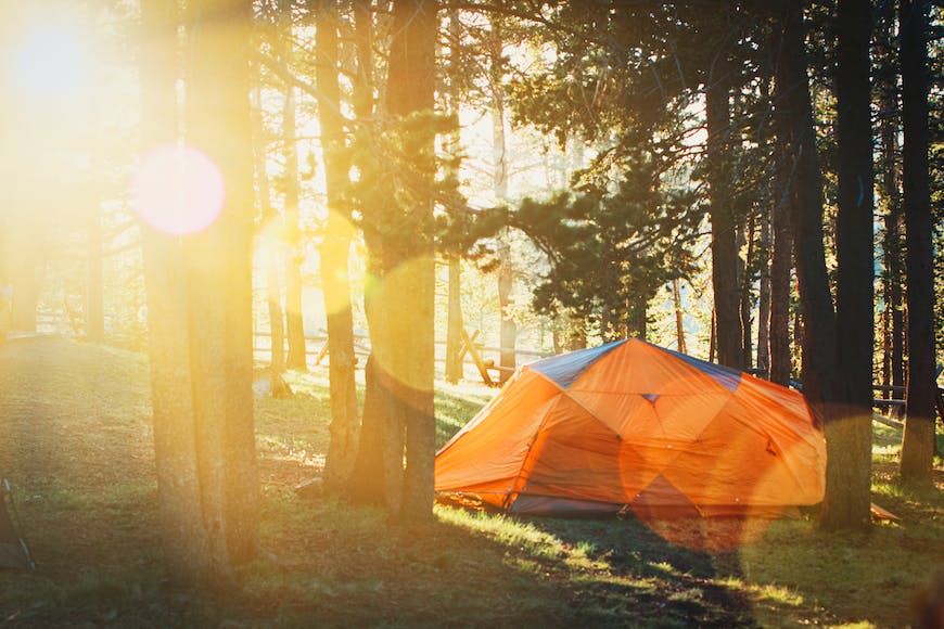 A tent in the woods with the sun shining on it.