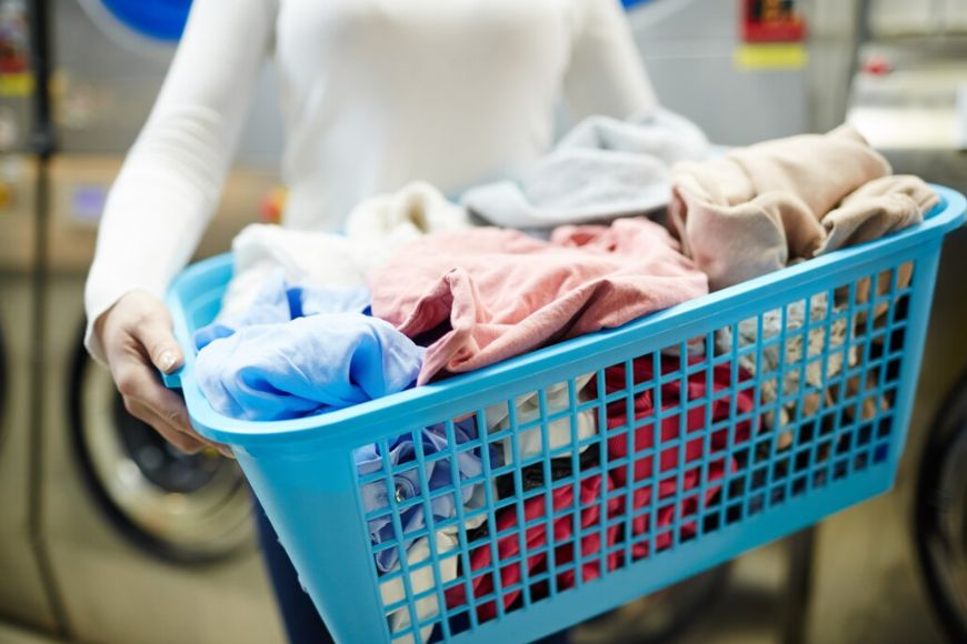 A woman is holding a basket full of clothes in a laundry room.