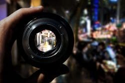 A person holding a camera lens in front of a city.