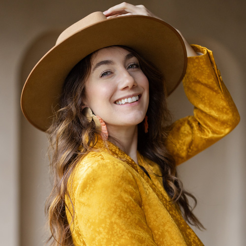 A woman wearing a yellow velvet jacket and hat.