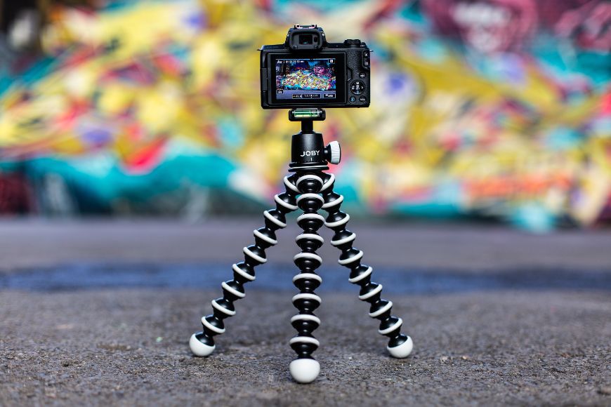 A camera is sitting on a tripod in front of graffiti.