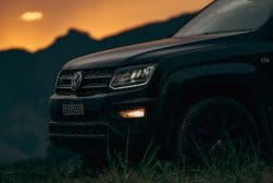 A black volkswagen atlas parked in a grassy field at sunset.