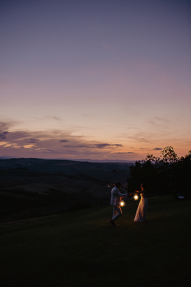 A bride and groom holding lanterns at sunset in tuscany.