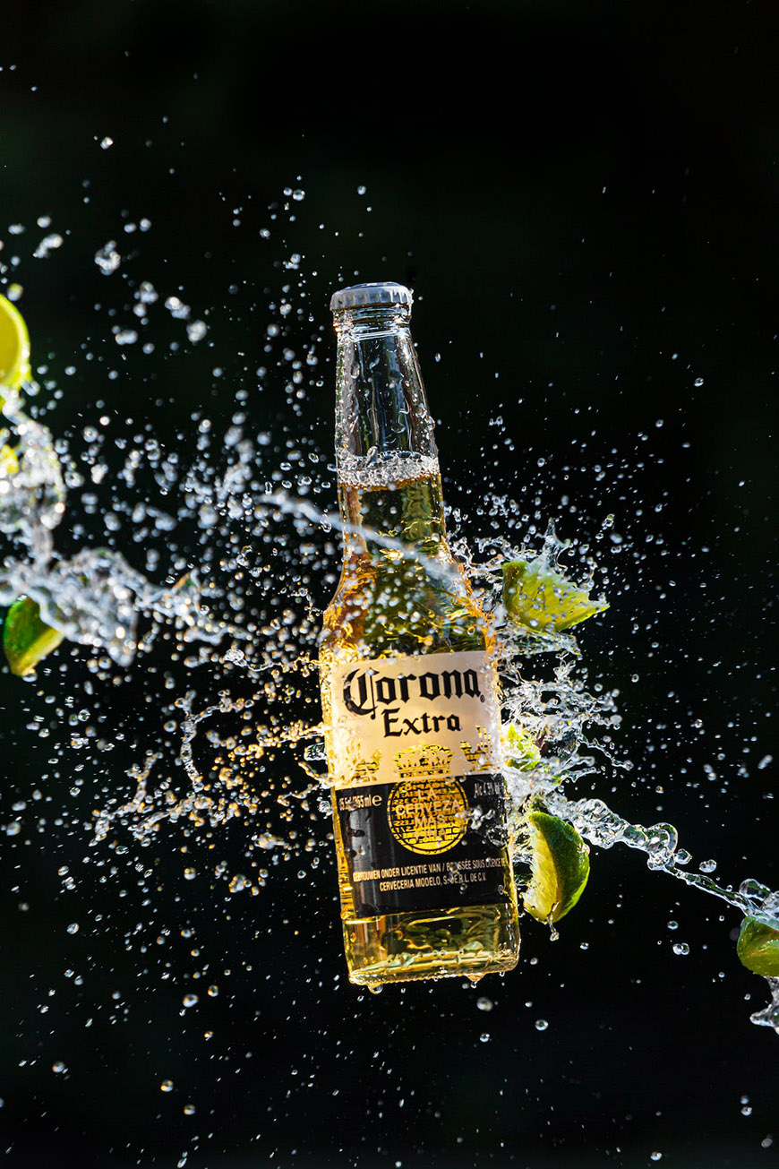A corona beer bottle is splashed with water.