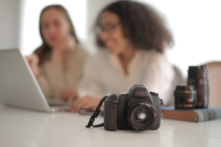 Two women sitting at a table with a camera in front of them.