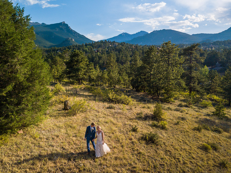 A bride and groom standing in a field with mountains in the background.