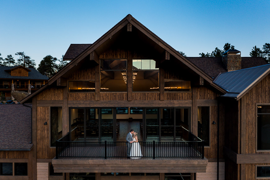 A bride and groom standing on the balcony of a lodge at dusk.