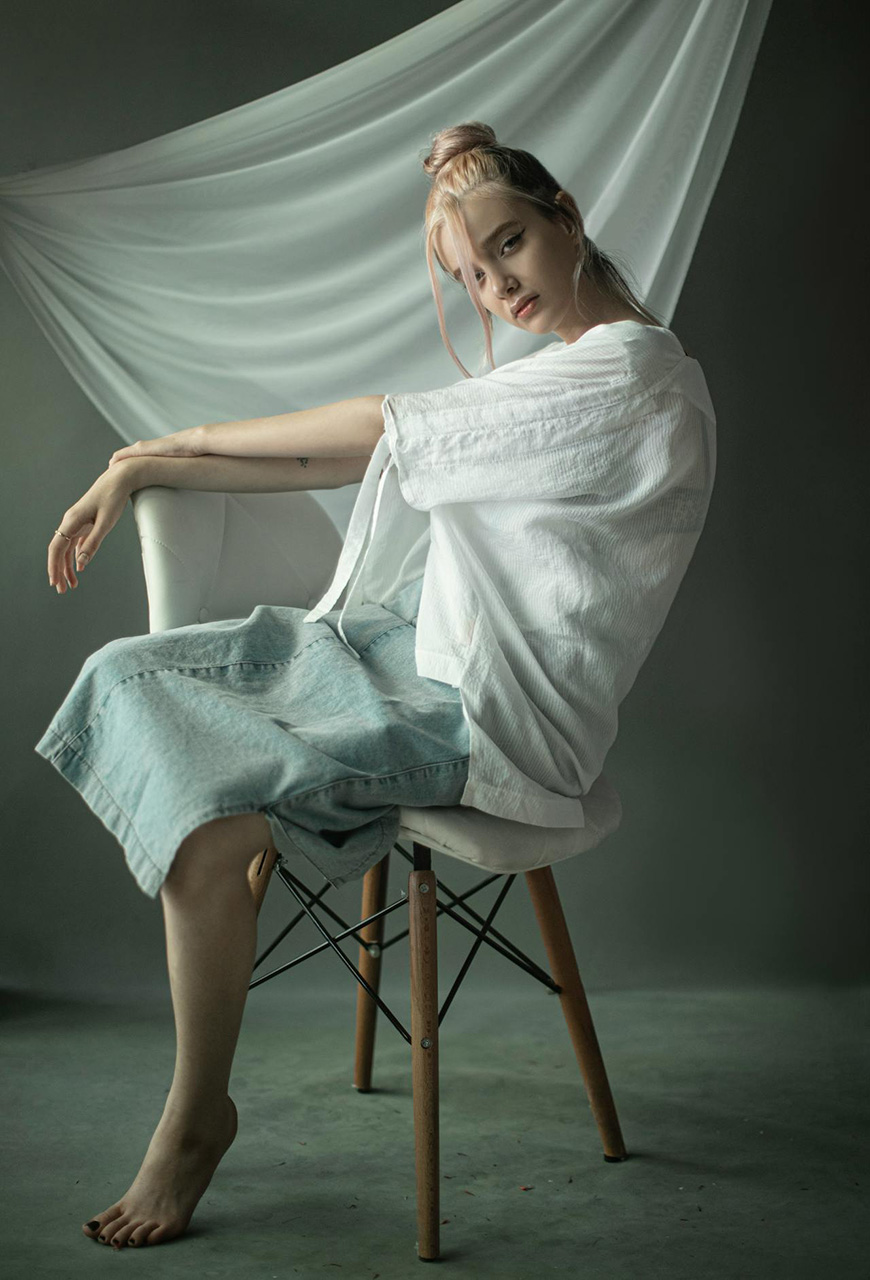 A woman sitting on a chair with a white shirt.