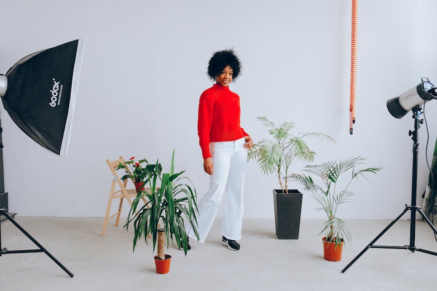 A woman in a red sweater standing next to a potted plant in a studio.