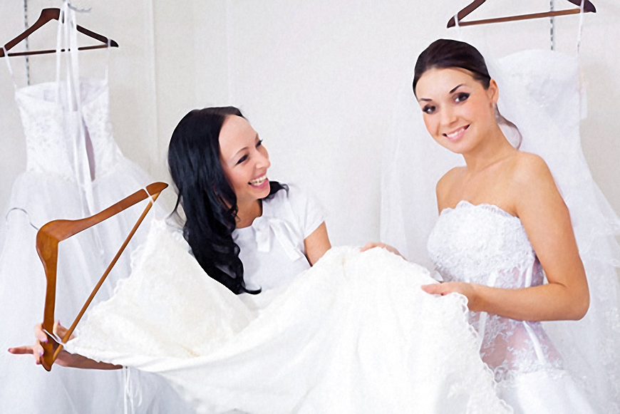 Two women looking at a wedding dress hanging on a rack.