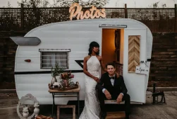 A bride and groom posing in front of a camper trailer.