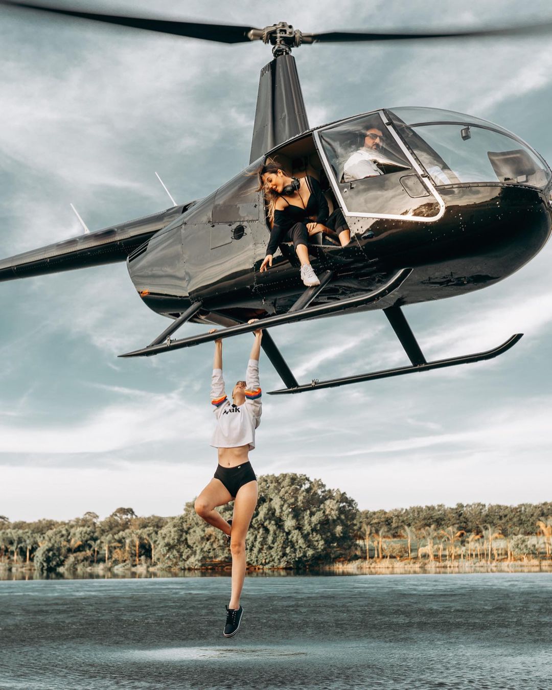 A woman is hanging from a helicopter in front of a lake.