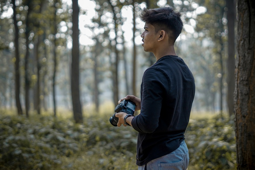 A man holding a camera in a wooded area.