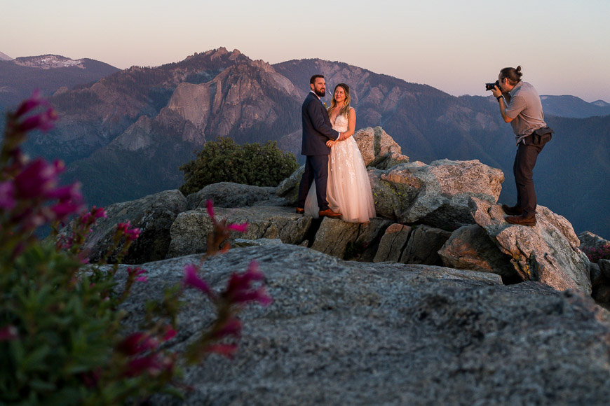 A bride and groom taking pictures on top of a mountain.