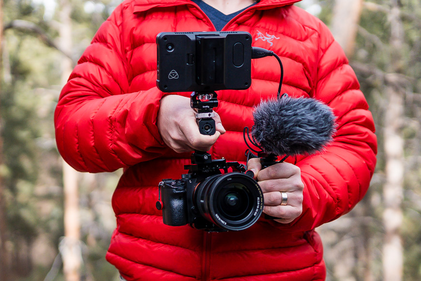 A man in a red jacket holding a camera and microphone.