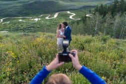 A bride and groom taking a picture of each other in the mountains.