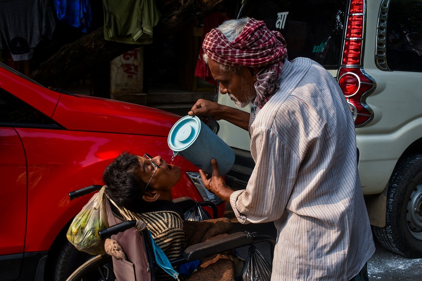 A man in a wheelchair giving water to a child in a red car.