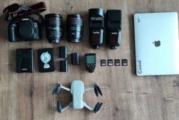A laptop, camera, and other items are laid out on a wooden floor.