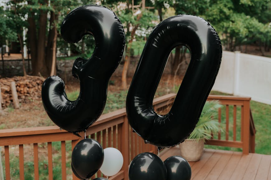 Black balloons with the number 30 on them on a deck.