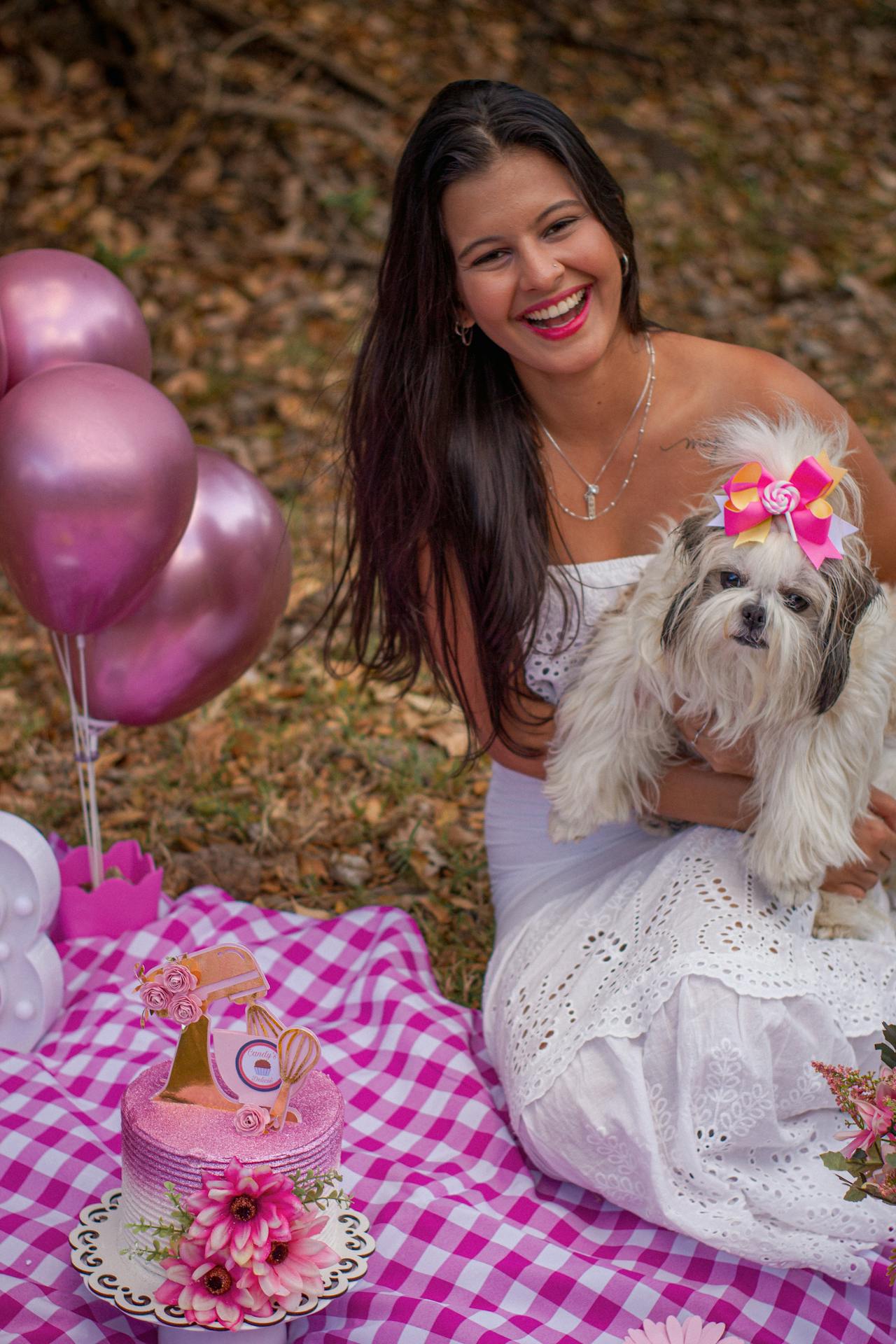 A woman with a dog sitting on a picnic blanket with balloons.
