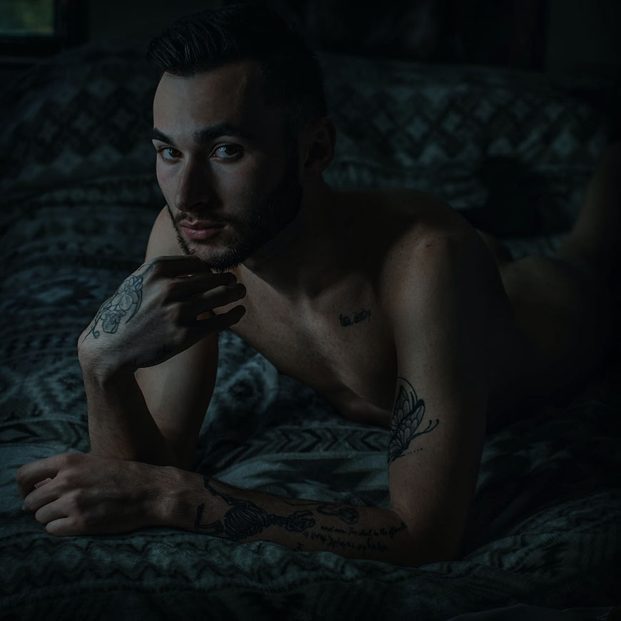 A man with tattoos laying on a bed.